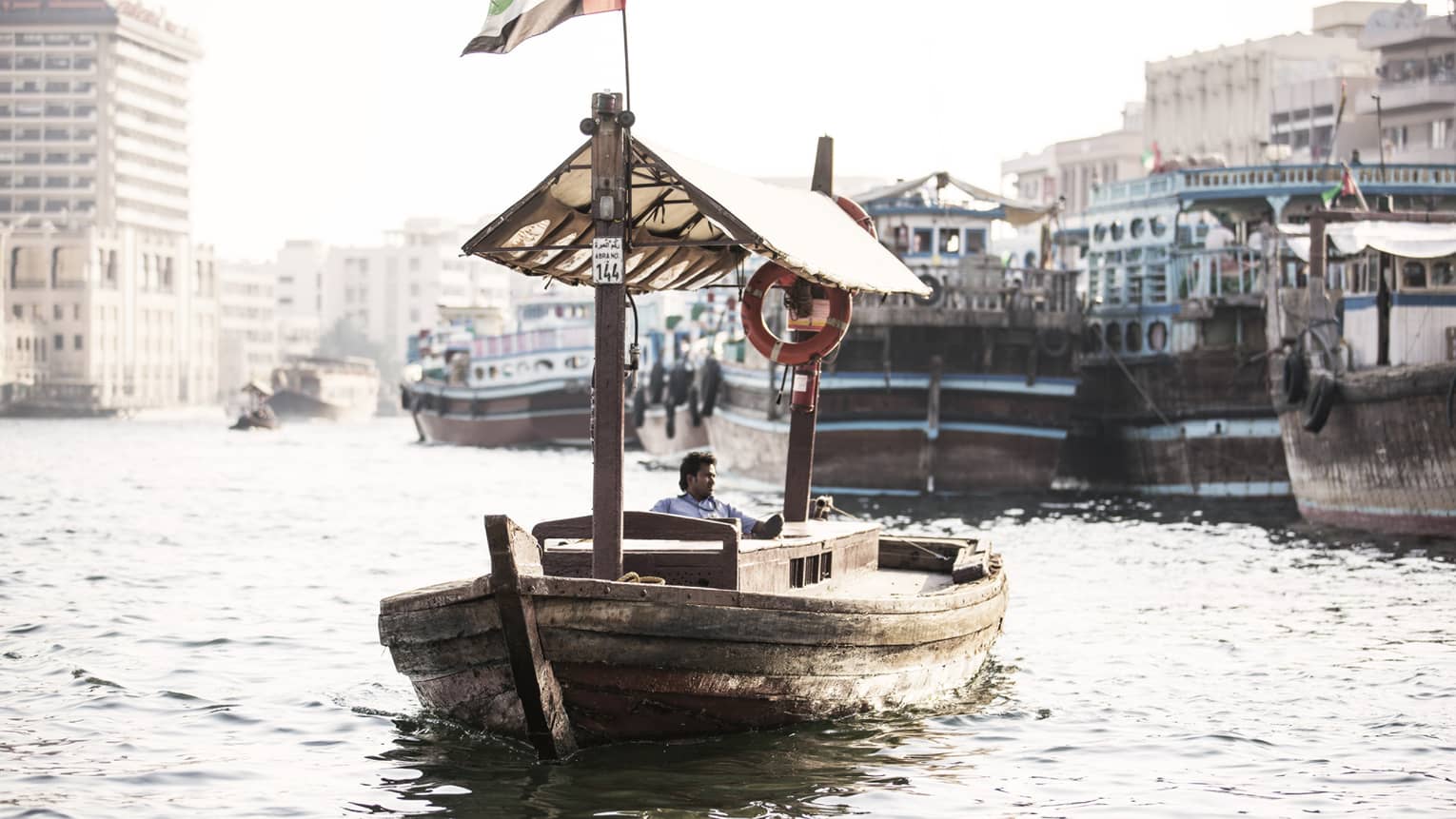 A small wooden boat flying the UAE flag as it sails down a small waterway. 