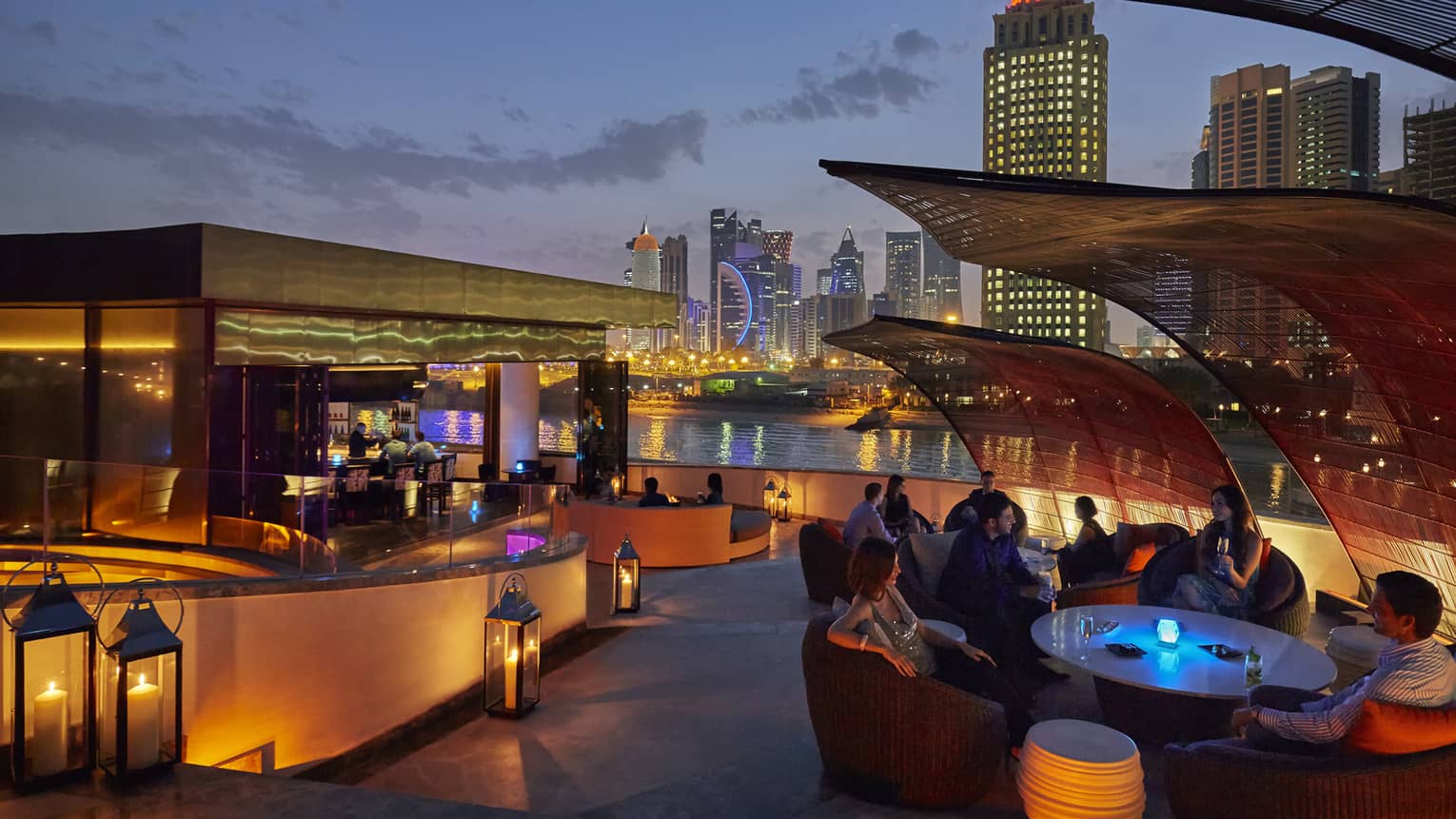 Nobu Doha patio at night with glowing lanterns around bar, table, city skyline in background