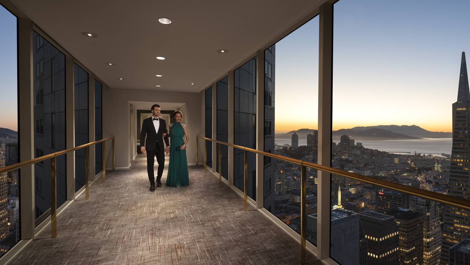 A man and woman in a suit and dress walking down a sky bridge.