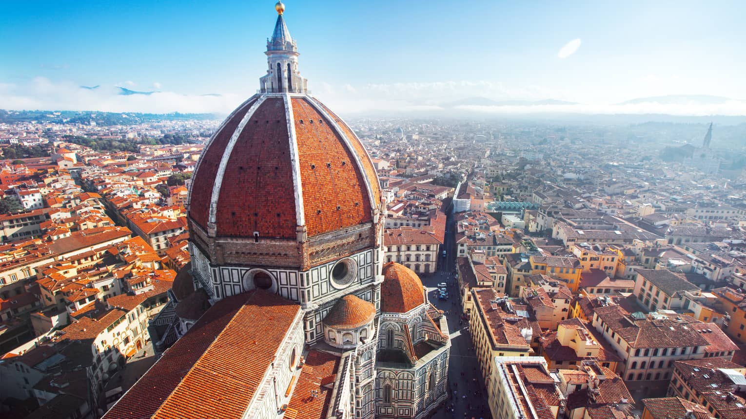 Aerial view of Florence city with red rooftops, Duomo cathedral dome against blue sky