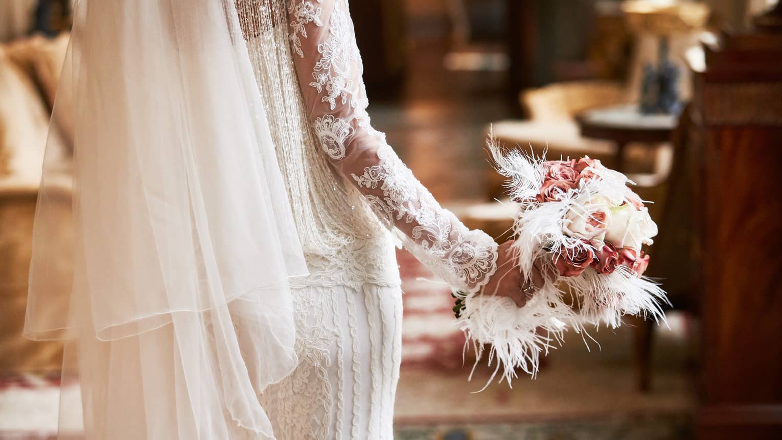 A close up of a bride's bouquet made up of white roses, pink flowers and white feathers