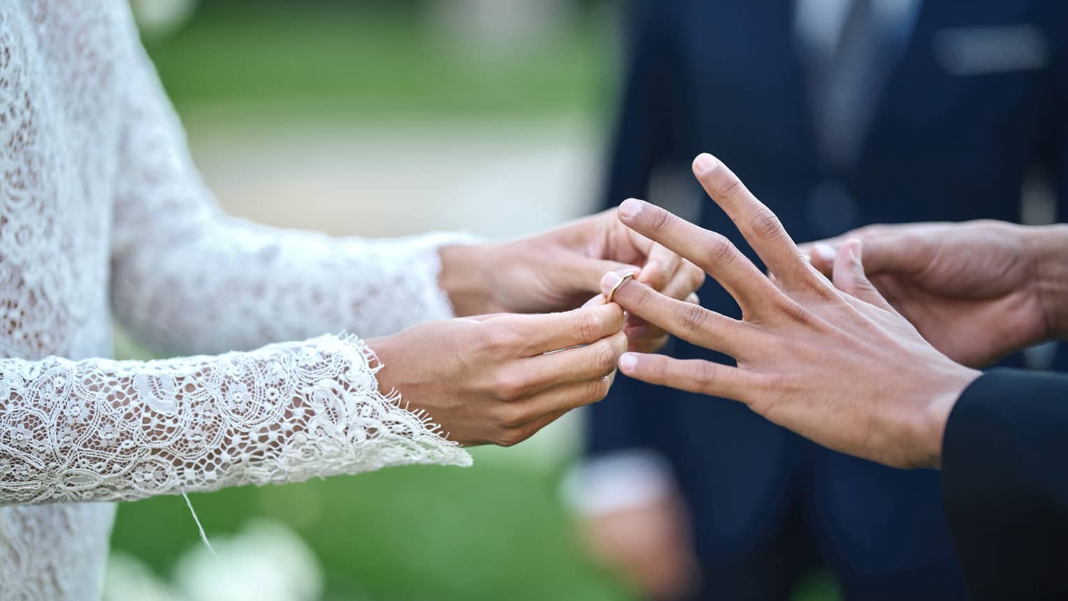 Close-up of bride's hands putting ring on groom's left hand