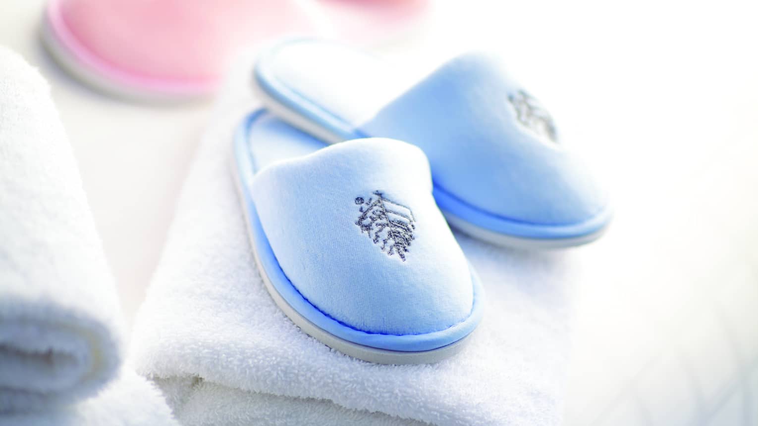 A pair of baby pink and baby blue kid's spa slippers and fluffy white towels