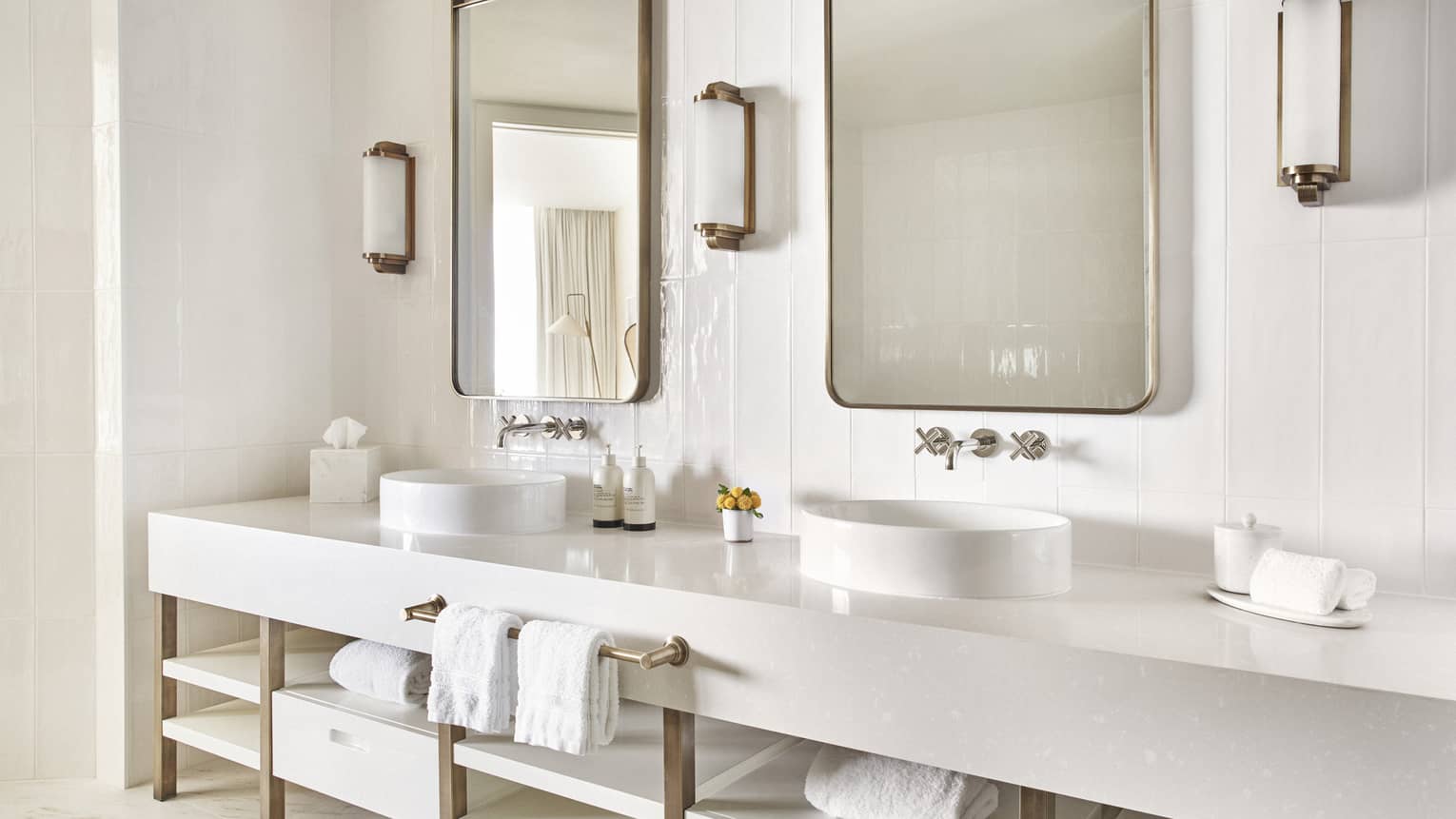 White bathroom with white double vanity, gold rimmed mirrors and wall sconces