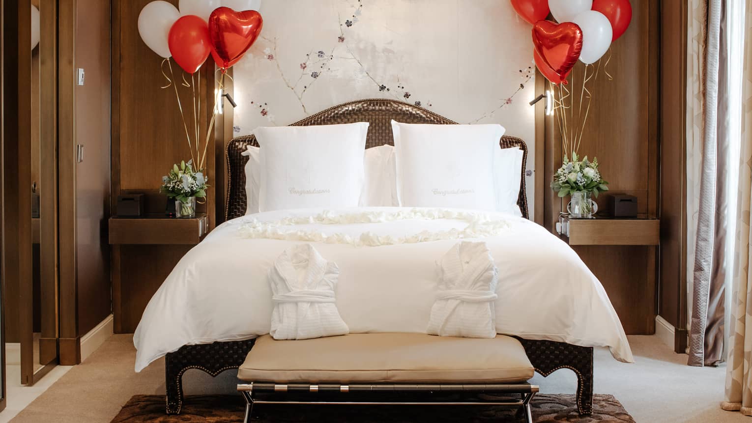 White Four Seasons bed against white wall, flanked with red and white balloons, and two white robes on foot bench