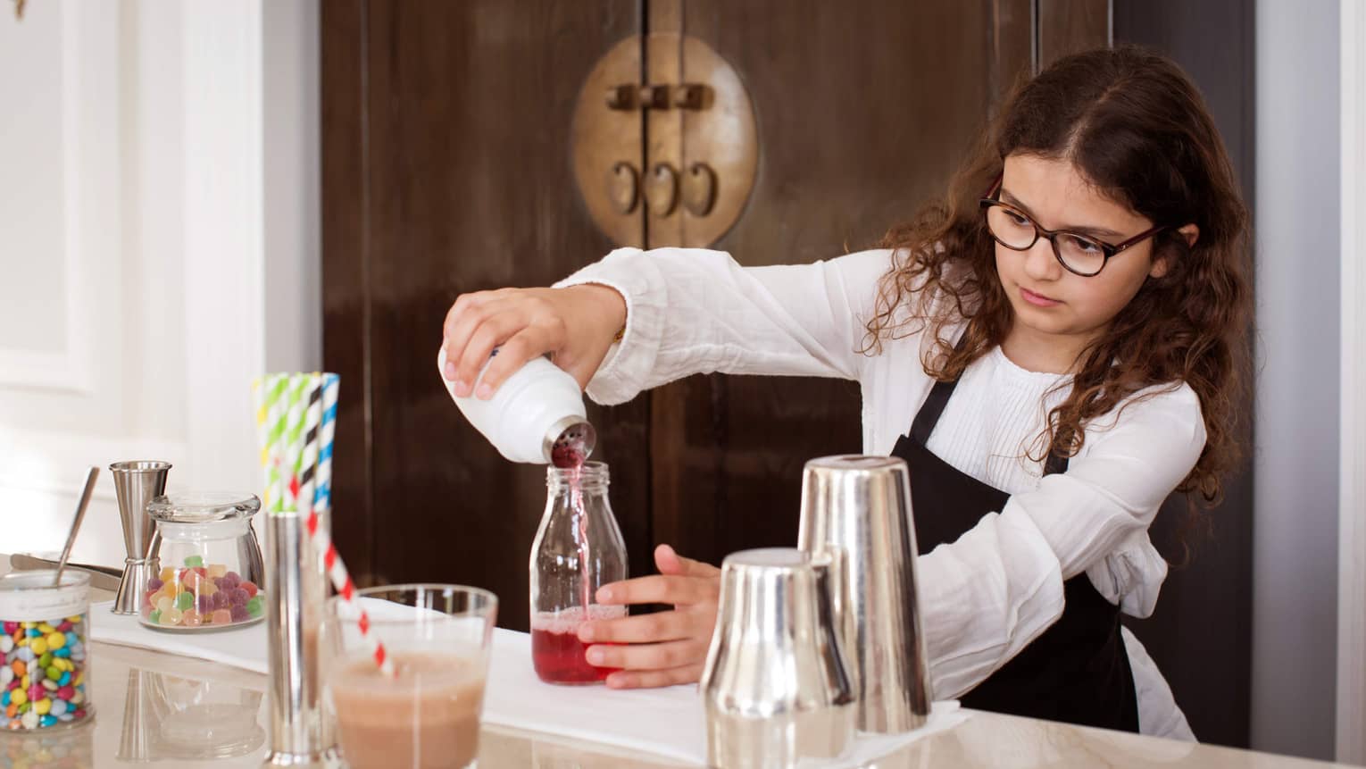 Girl with dark hair and glasses wearing apron, mixing mocktails