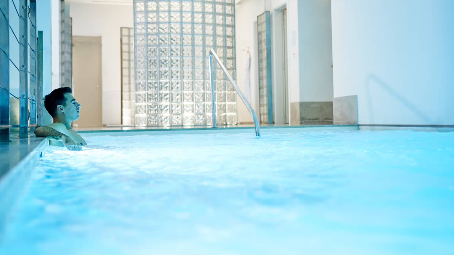 Man leans back in indoor pool with blue illuminated water