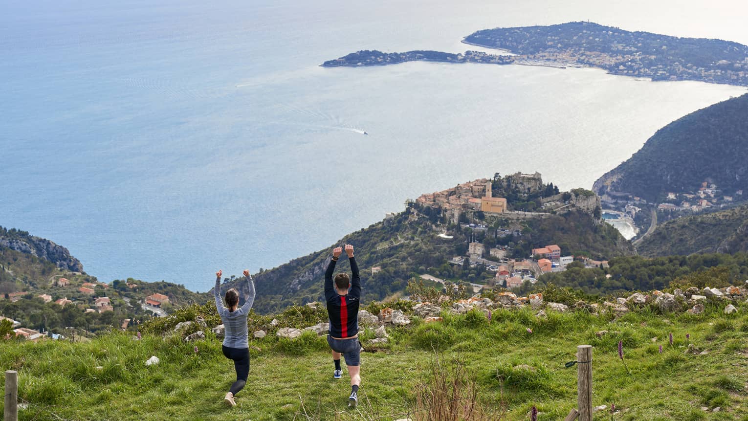 Rear view of woman and man doing yoga on green hilltop overlooking Mediterranean Sea