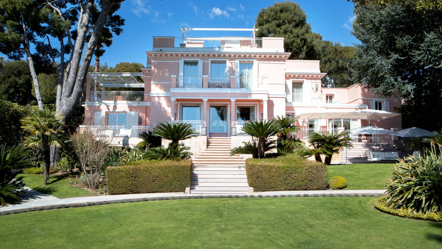 Manicured gardens, steps up to large three-storey pink Villa Rose-Pierre