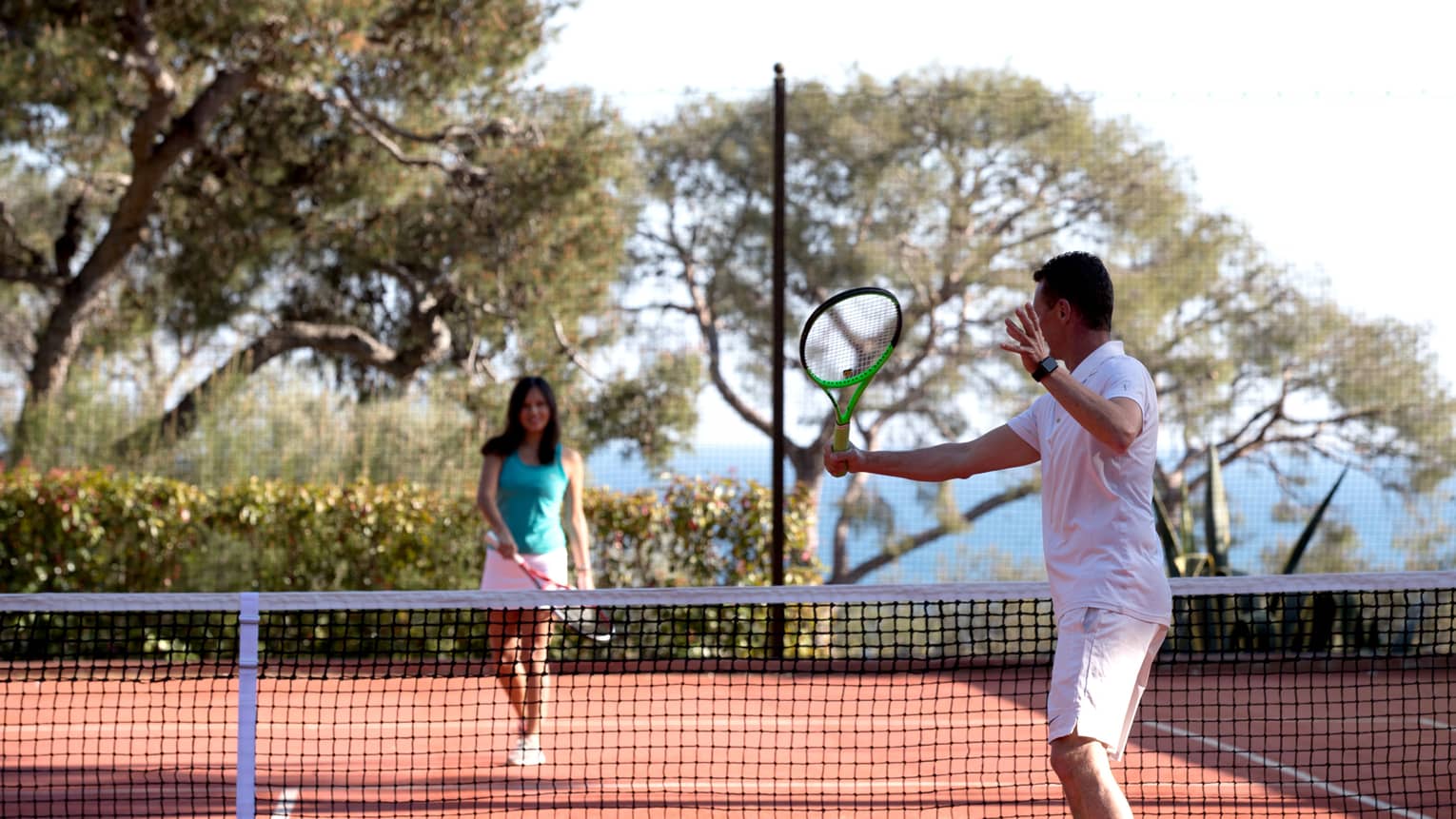 Man swing tennis racket, woman on other side of net