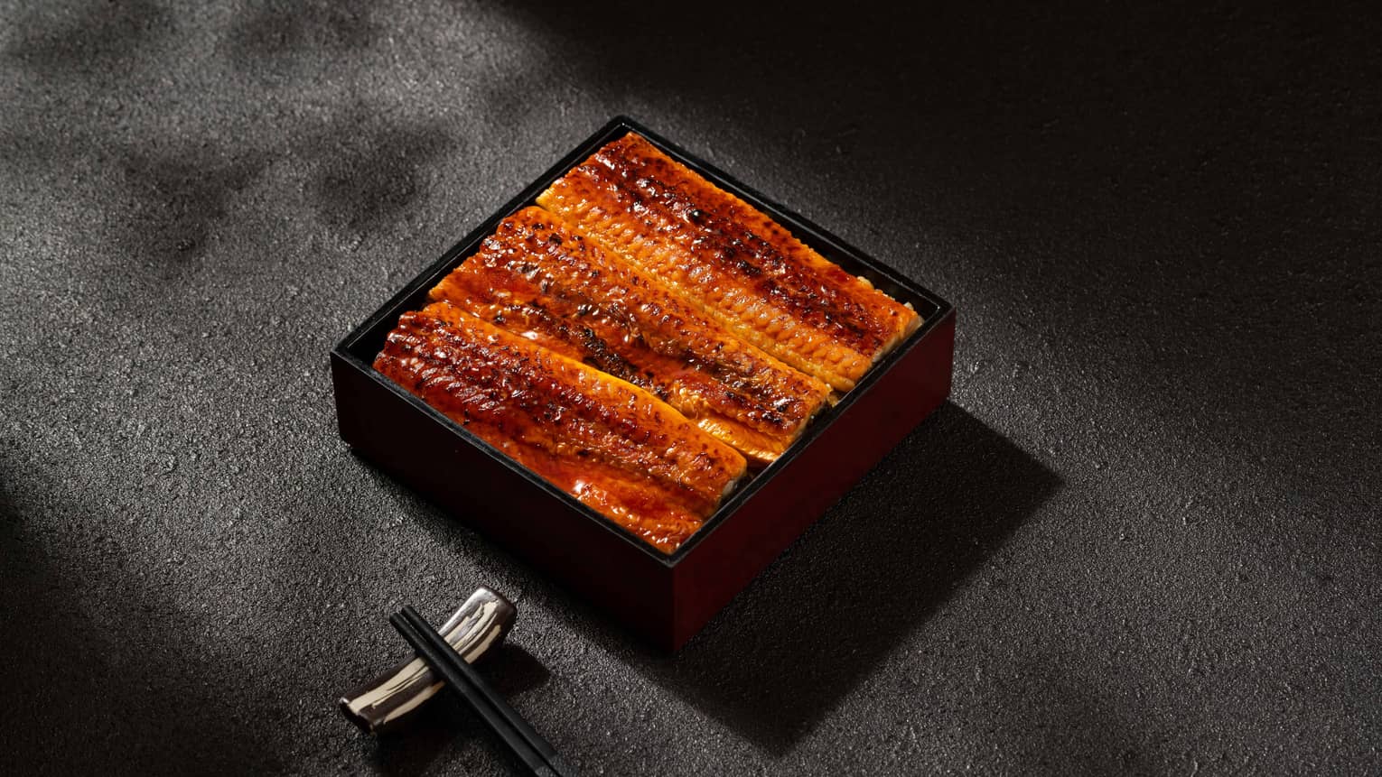 Grilled eel rice box with black chopsticks nearby