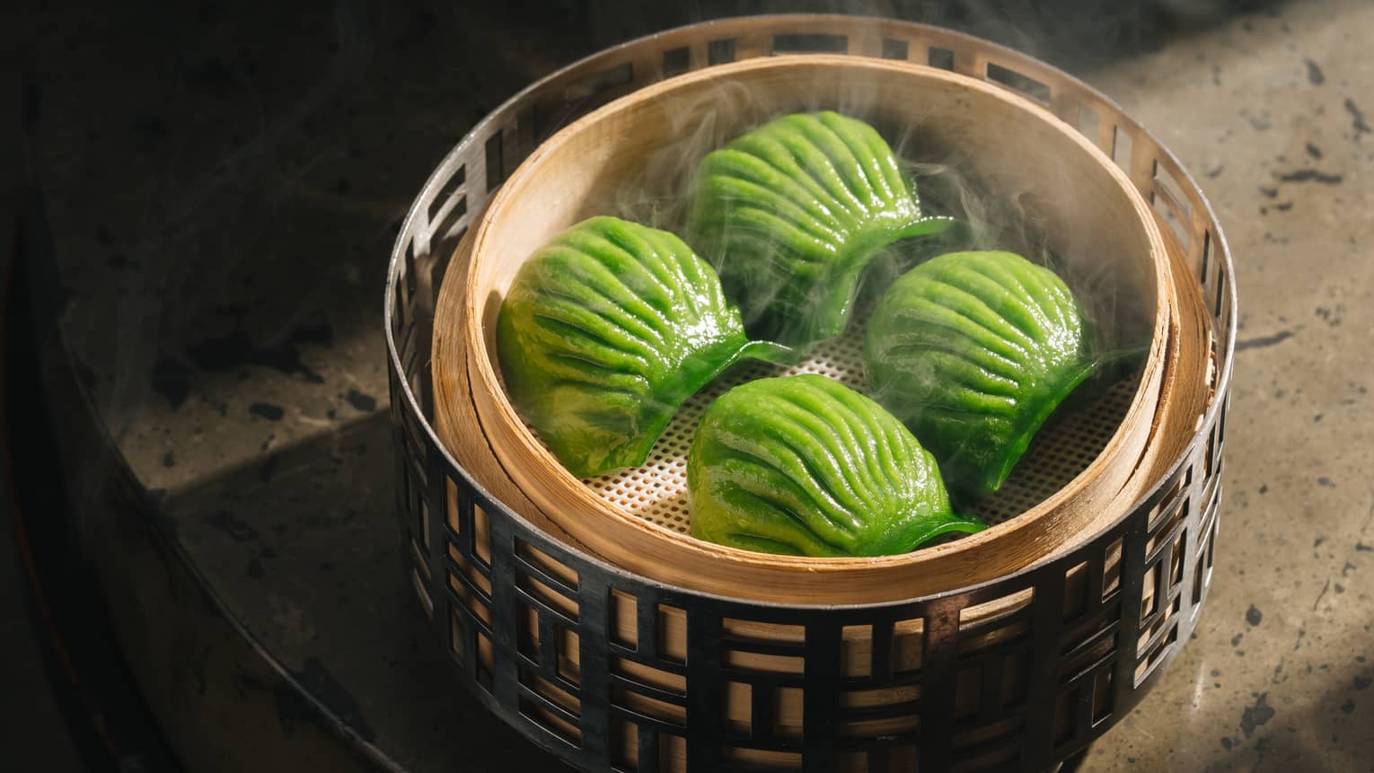 Four green shell-shaped dumplings in traditional bamboo steamer