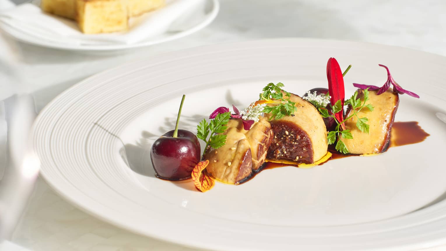 Delicately arranged foie gras garnished with microgreens; deep red, magenta and white flower petals; balsamic; and a cherry.