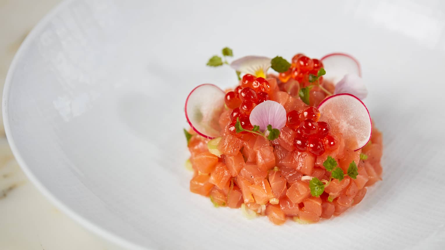 Raw salmon cut into small pieces with fish roe and herbs.