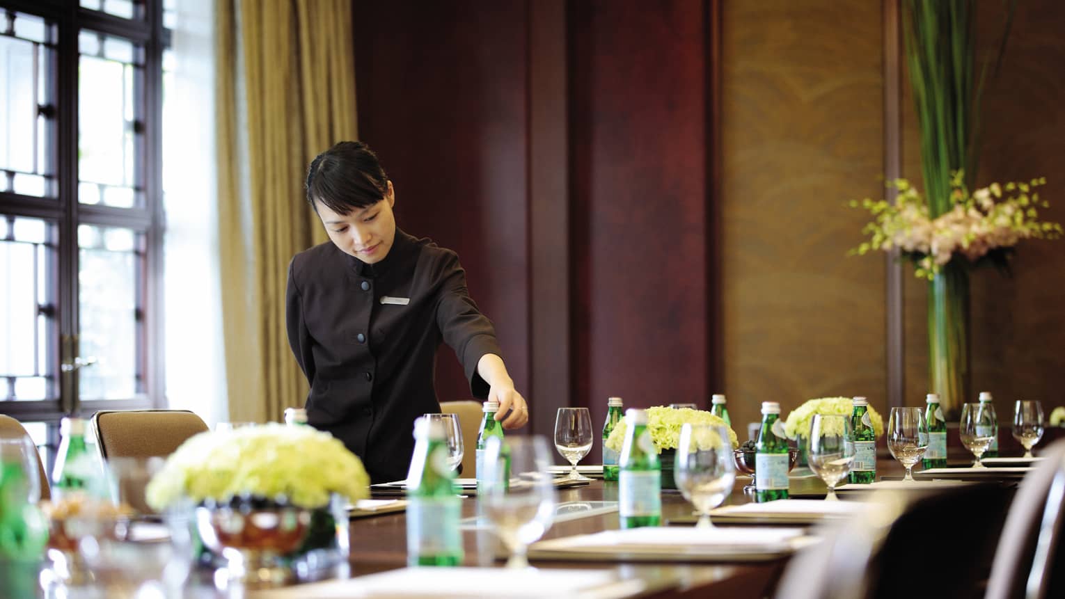 Restaurant server sets green sparkling water bottle on long meeting table