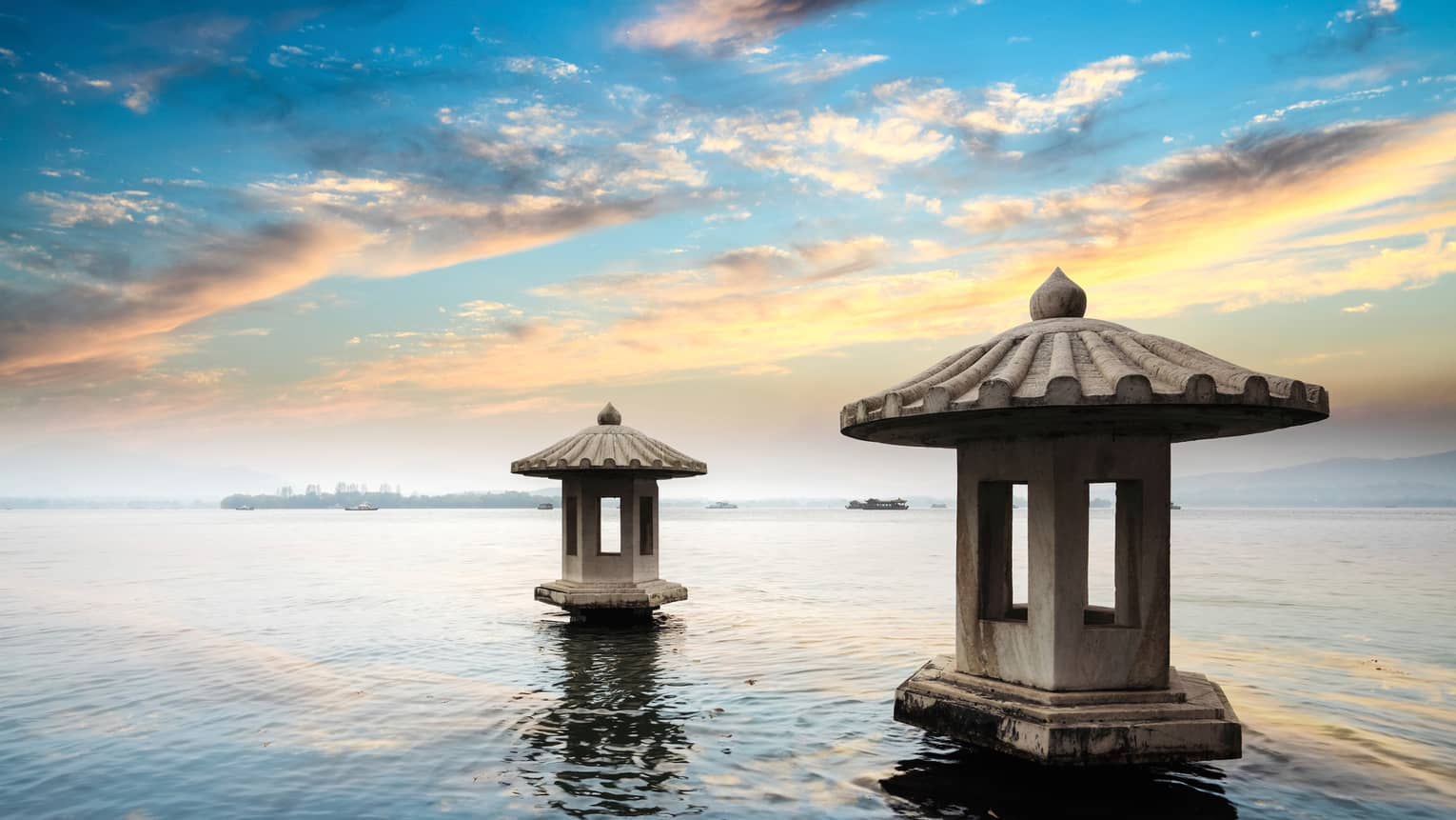 Sunset reflected on West Lake, two cement pagoda structures in water 