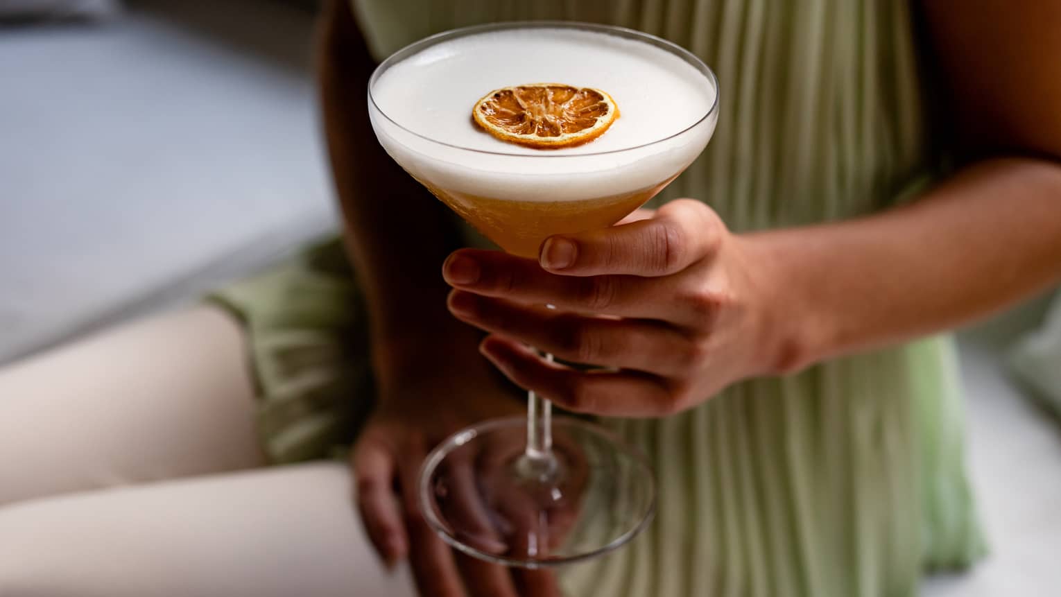 A woman's hand holds a cocktail with slide of dried orange on top