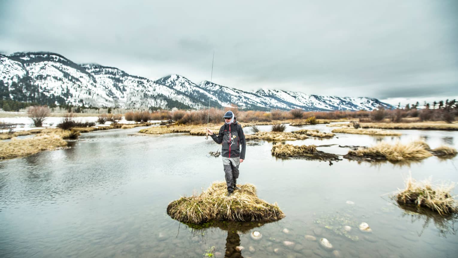 A man standing on a small piece of land surrounded by water holding a fishing rod.