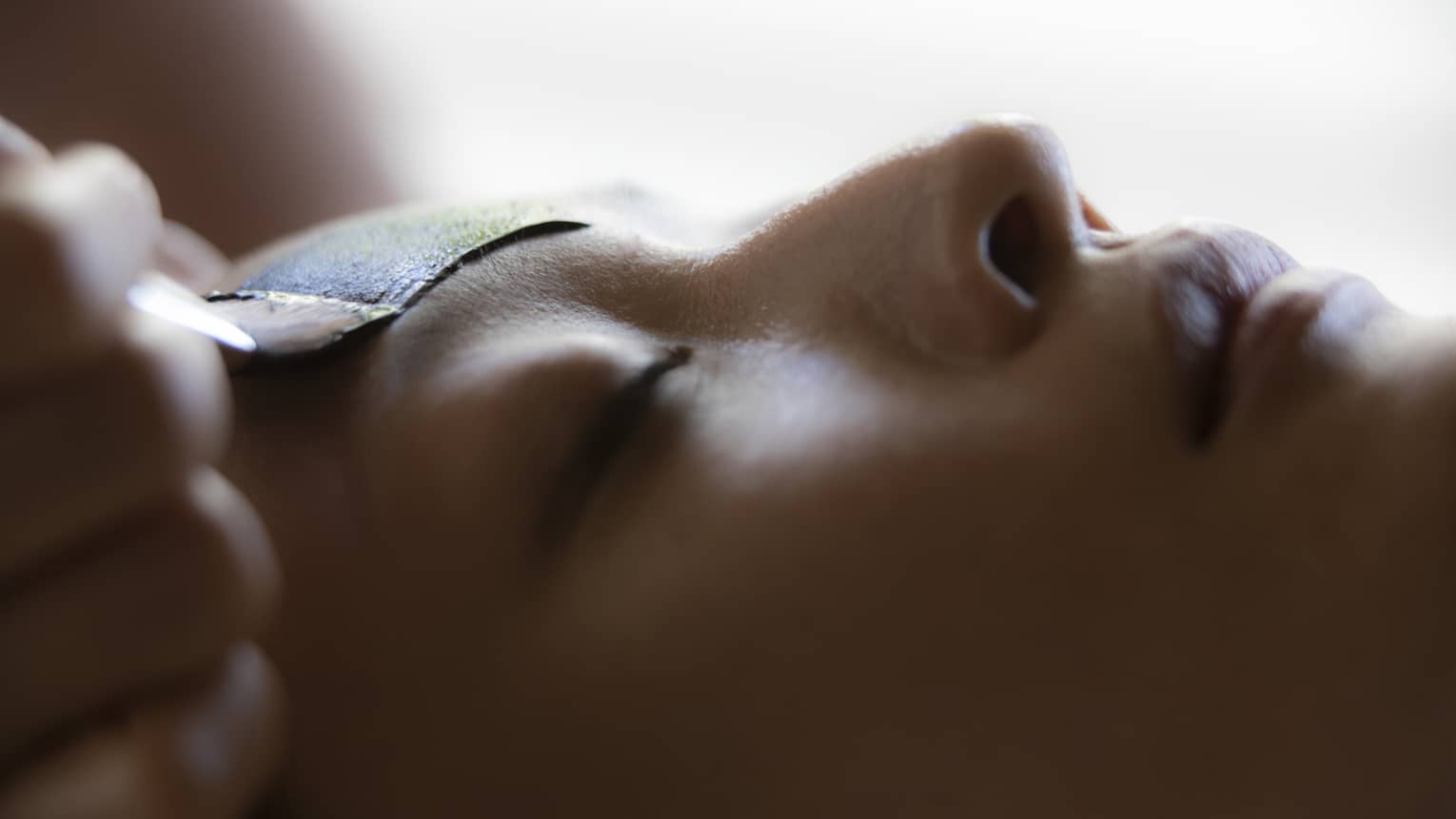 Close up of woman's face as a spa therapist paints on a facial mask on her forehead