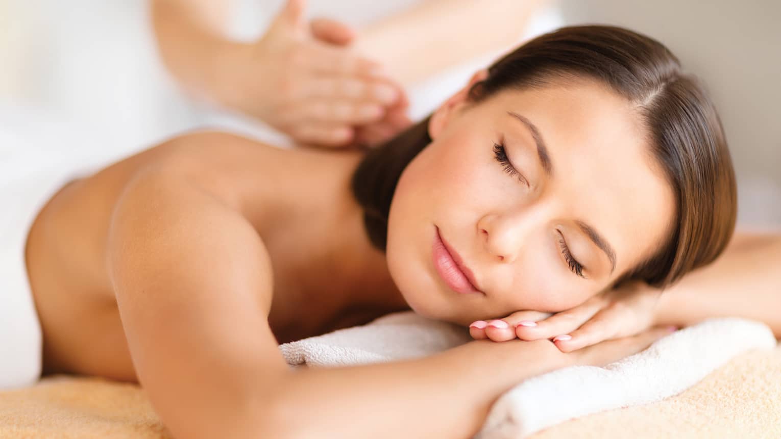 Woman lies on massage table, closes eyes. rests head on arms as spa staff massages back