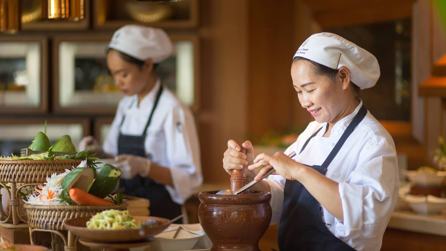 Two chefs in uniform prepare authentic Thai cuisine dishes at counter with fresh vegetables