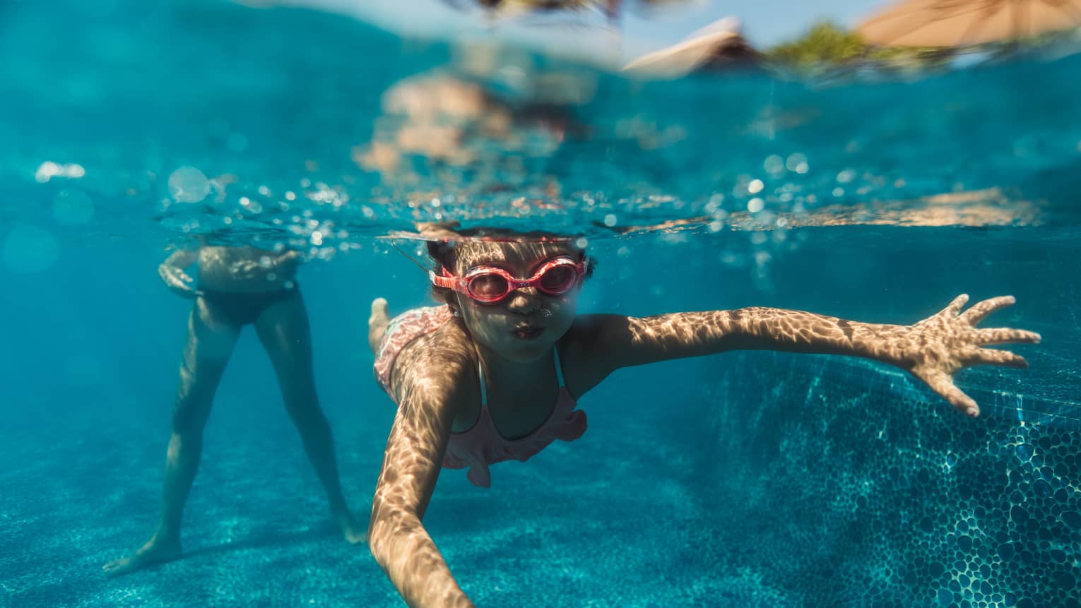 A young boy snorkeling in a pool with red goggles on.