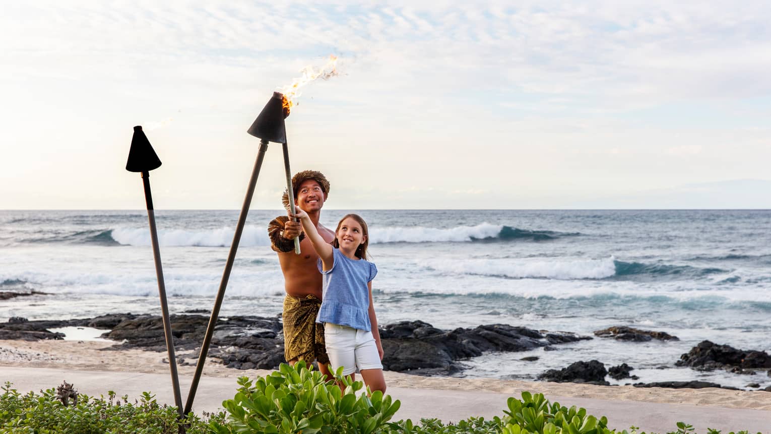 A father and daughter lighting lanterns along a beach shore together.
