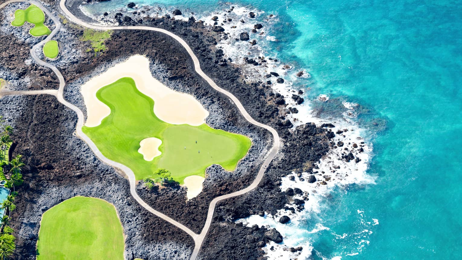 Aerial view of green golf course, black lava rock and turquoise water