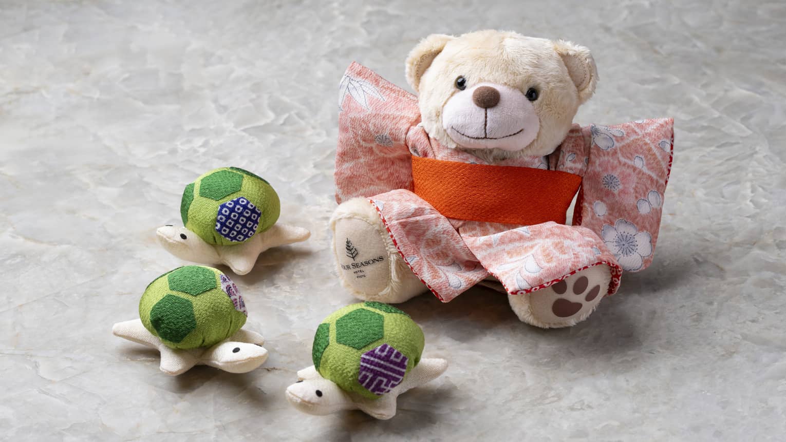 Cream-coloured stuffed bear in kimono and three stuffed turtles with green patterned shells