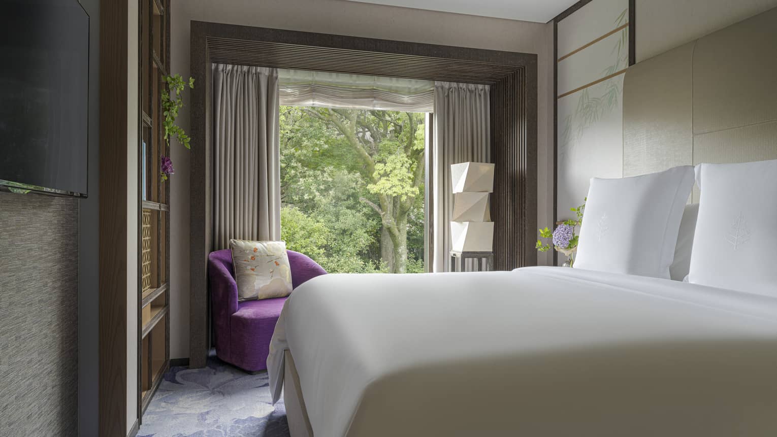 Serene bedroom at luxury hotel with king bed, dark pink arm chair and garden view