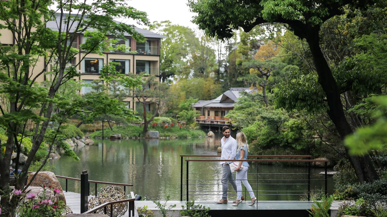 Couple walks across small bridge over pond surrounded by trees