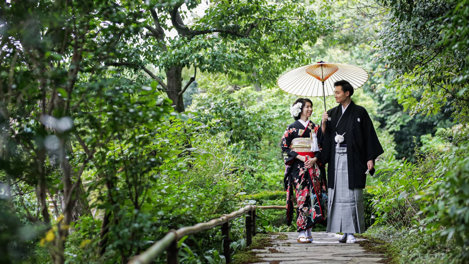 Couple wearing traditional Kyoto dress walk down stone path surrounded by trees