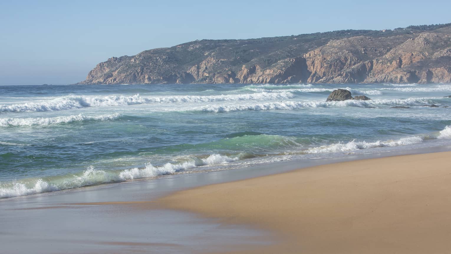 Blue waves roll onto shore on serene Guincho Beach in Portugal 