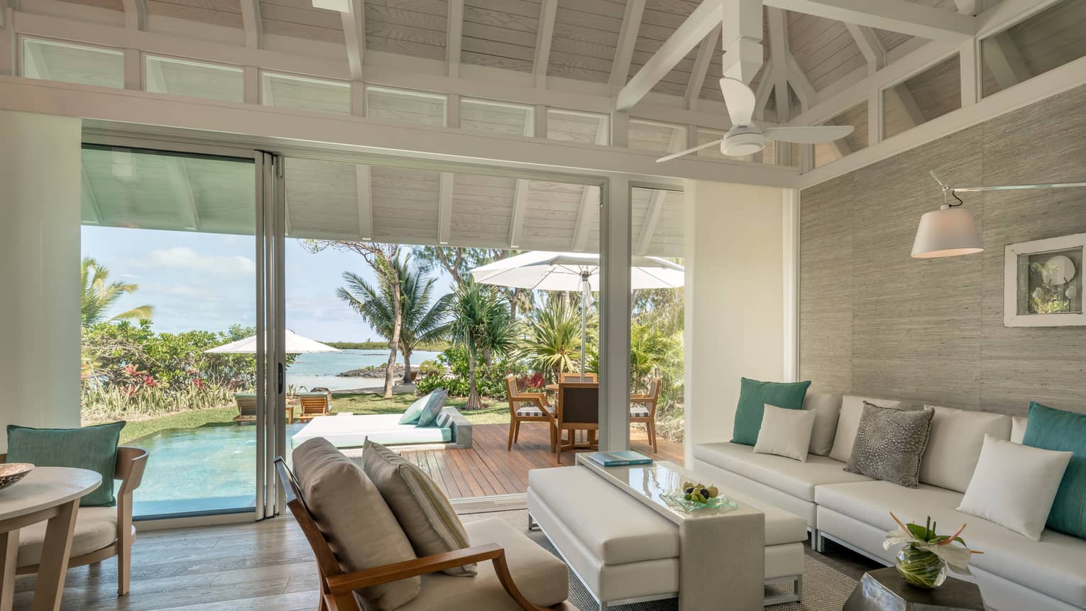 Sanctuary Beach Pool Villa with long white sofa, ottoman, chair, open glass wall to patio