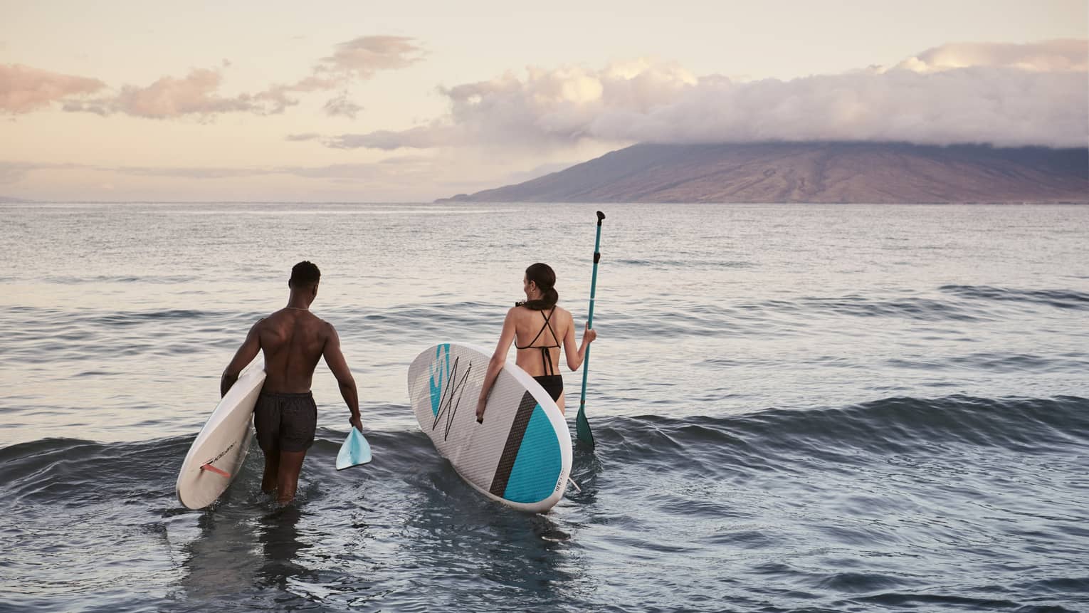 Man and woman carry SUP paddleboards into ocean in Maui