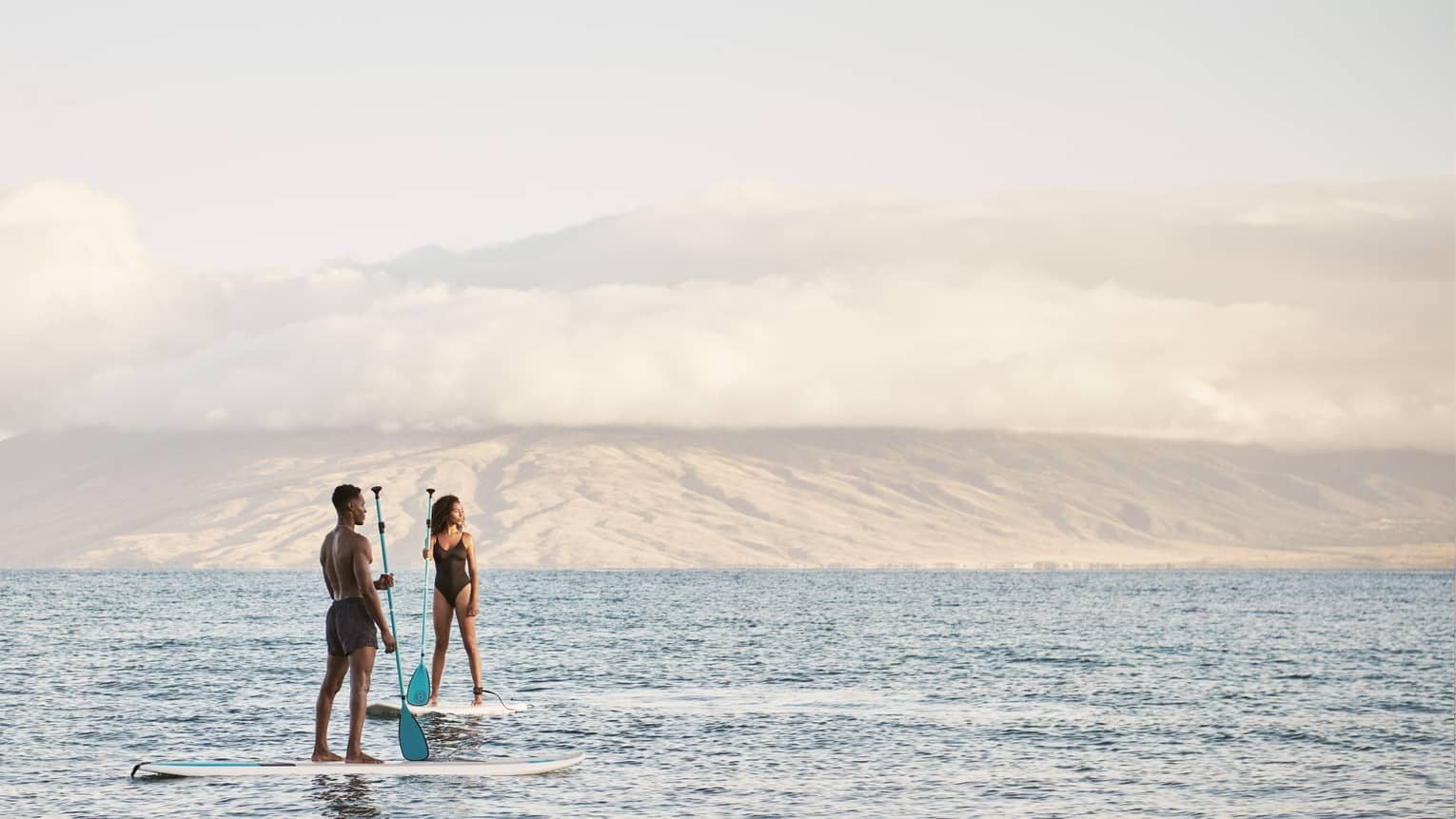 Man and woman stand on SUP paddleboards in the ocean in Maui