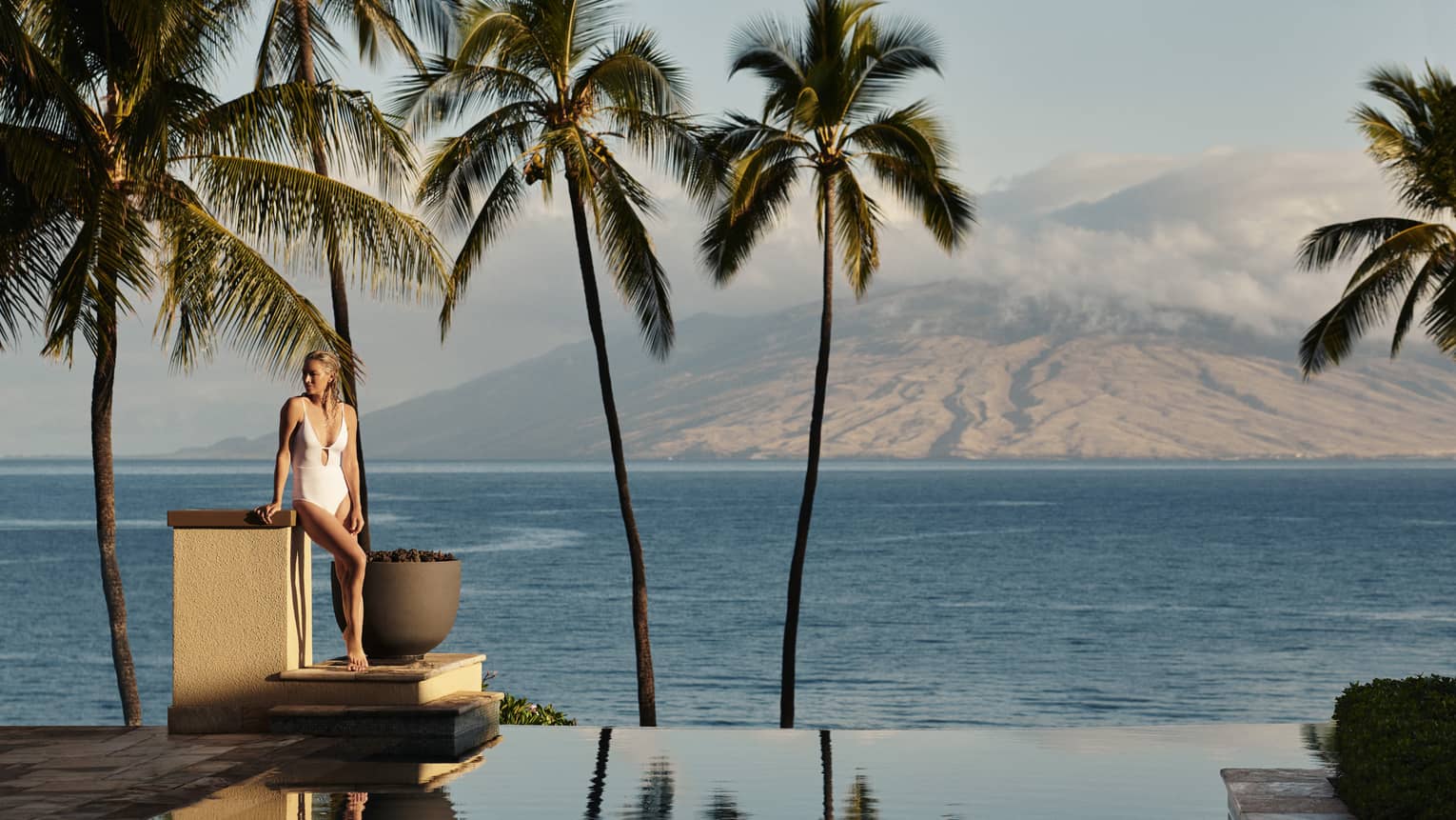 Woman stands on edge of infinity pool in Maui