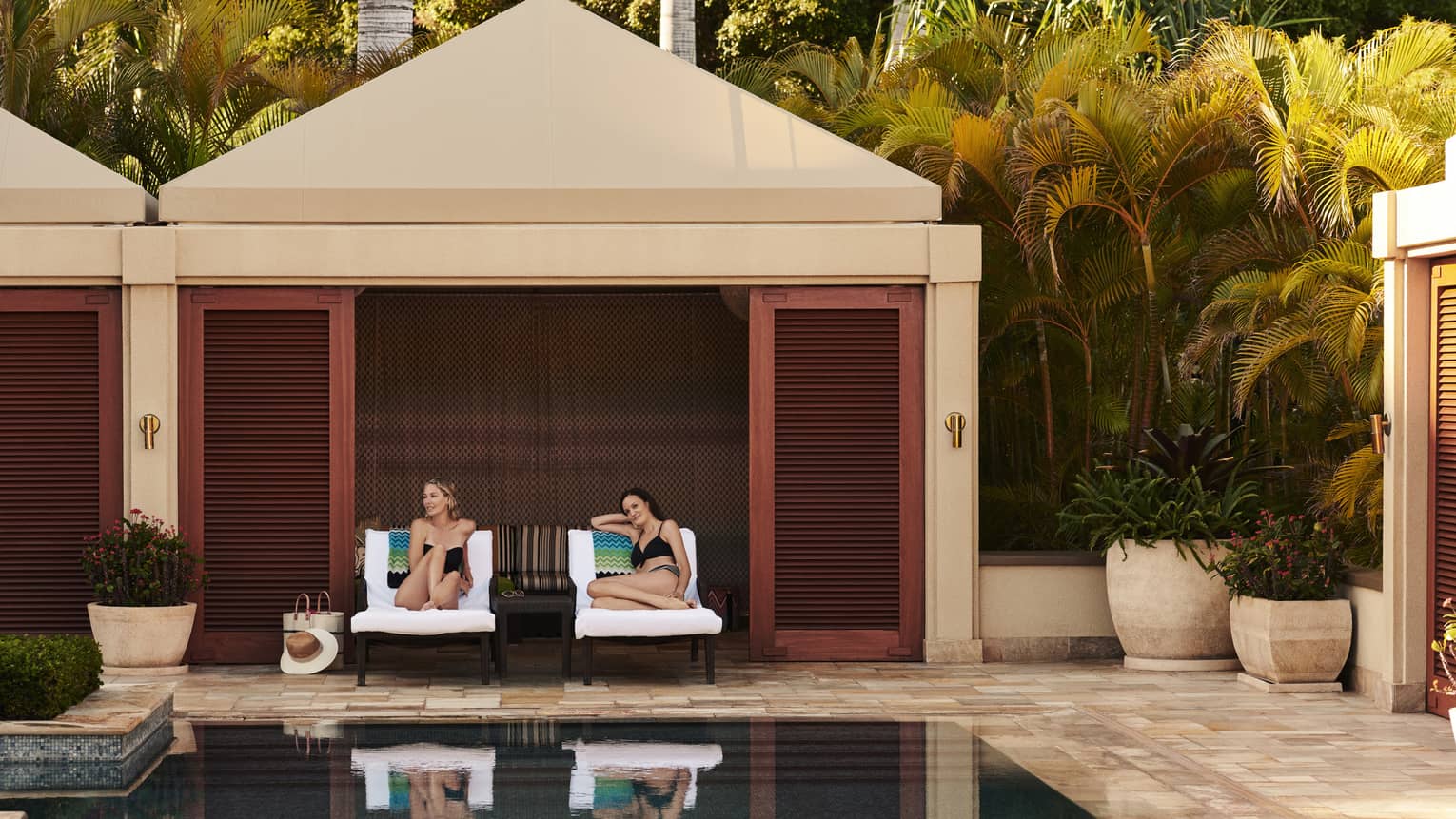 Two women on lounge chairs under poolside cabana