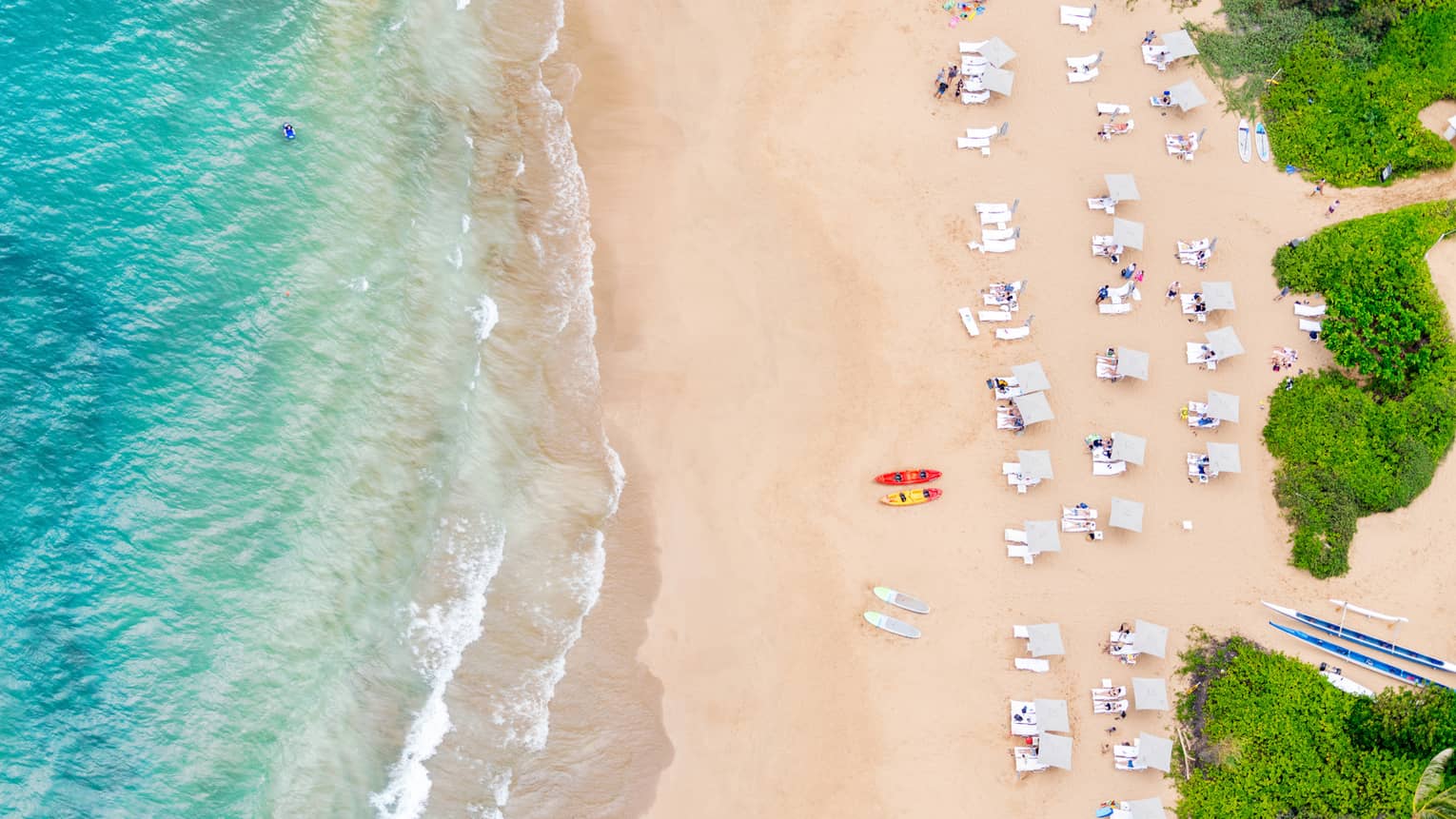 Aerial shot of a turquoise ocean and beach with white lounge chairs