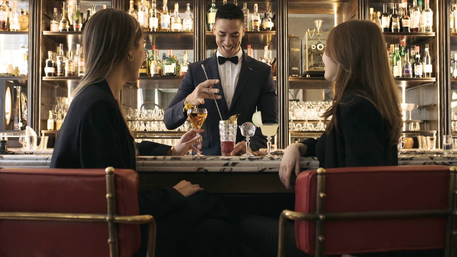 Two women sitting at a bar being served by a bartender.