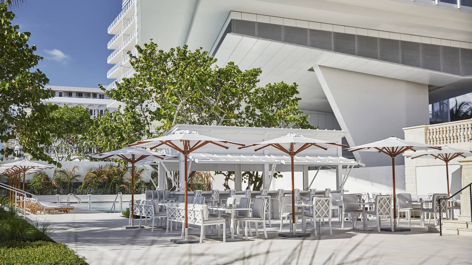 A large outdoor seating area of white chairs and tables covered with white umbrellas.