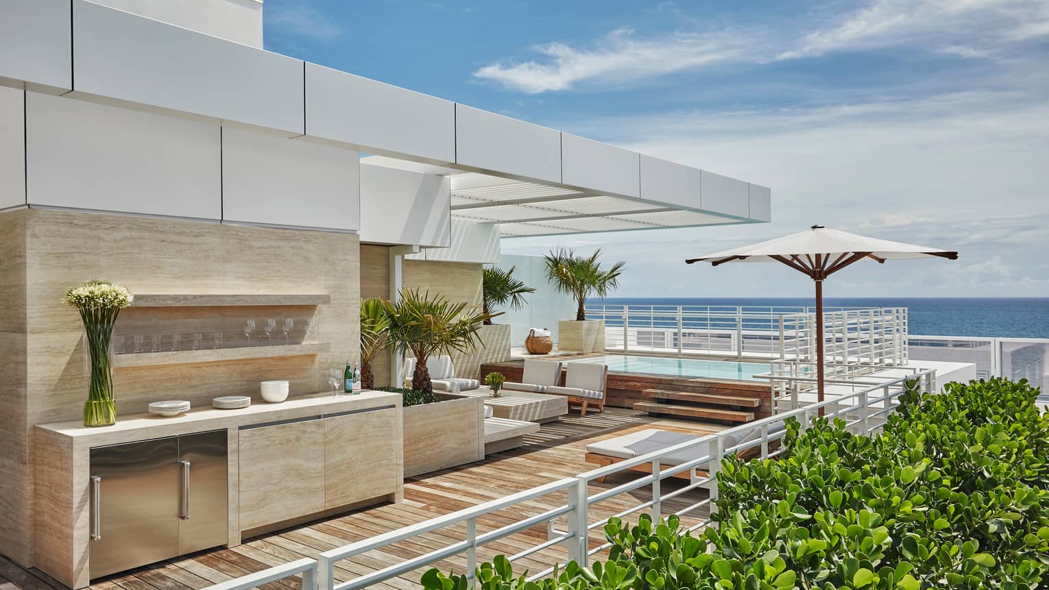 Marble outdoor bar and kitchenette with glasses, flowers, white sofas on modern rooftop patio with ocean views