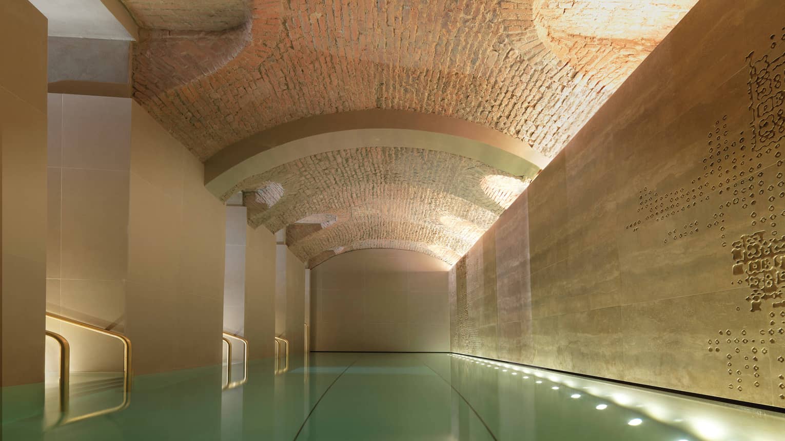 Indoor lap swimming pool with gold railings under curved stone ceiling