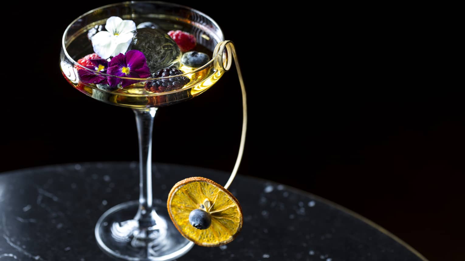 Cocktail glass. liquor garnished with small flowers, berries and dried orange wheel