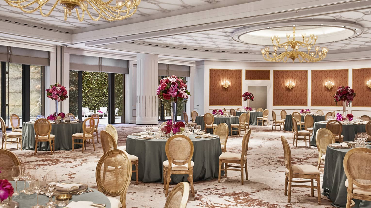 Ballroom with round tables, gold chairs, gold chandeliers, pattern carpeting, wall sconces