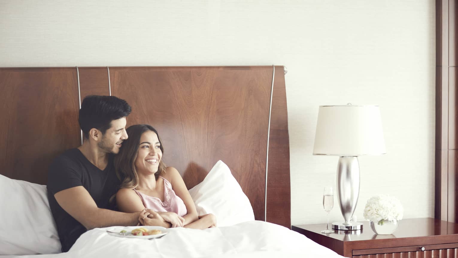 Couple cuddles in bed in modern hotel room