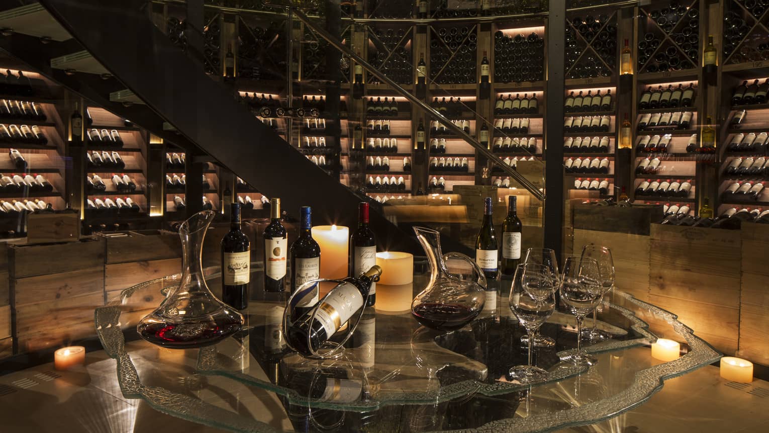 Bottles of wine are arranged for a tasting within an expansive, candlelit wine cellar
