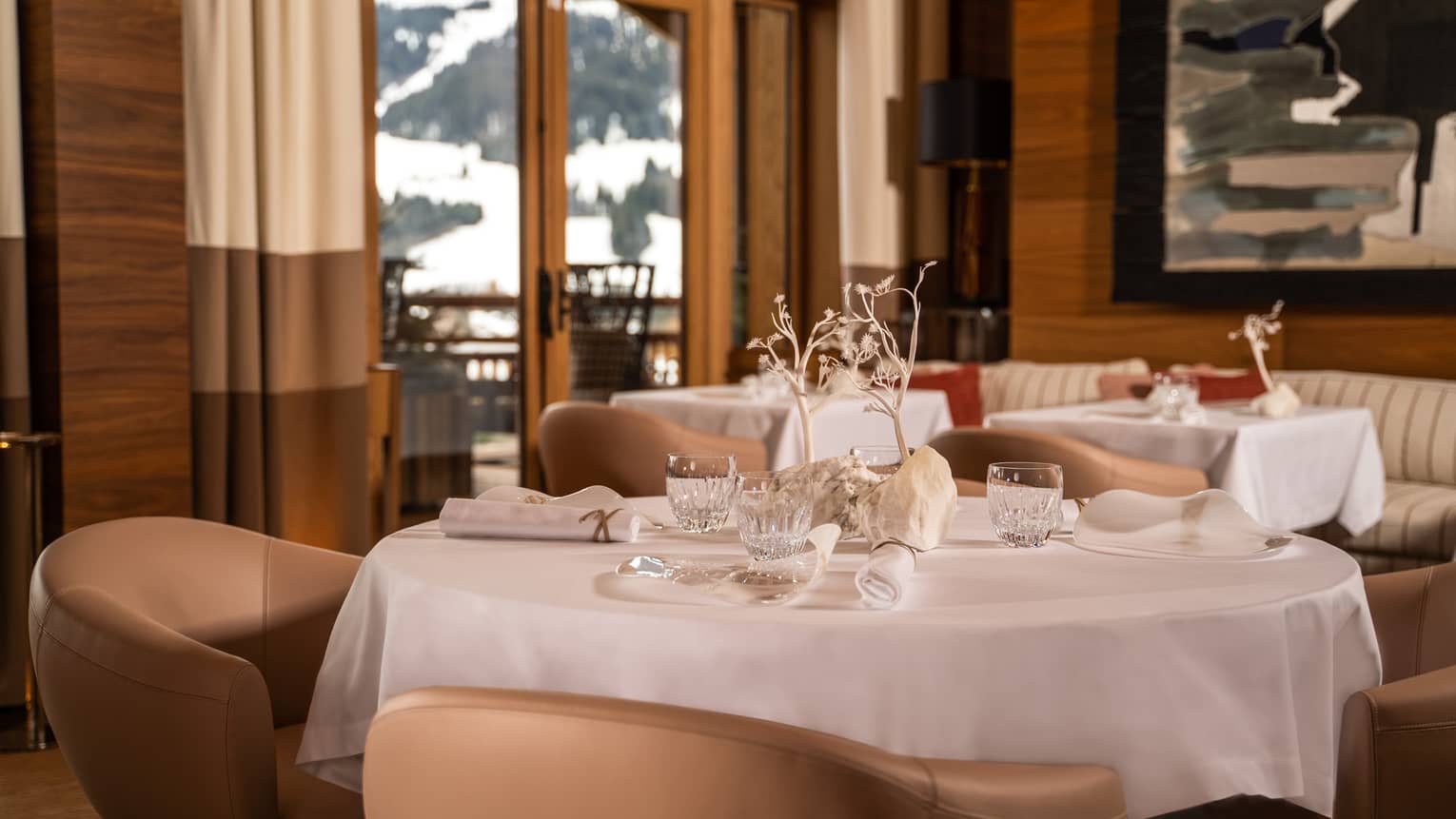 Round tablecloth-clad dining table and tan round chairs in wood-panelled restaurant with snowy mountain view