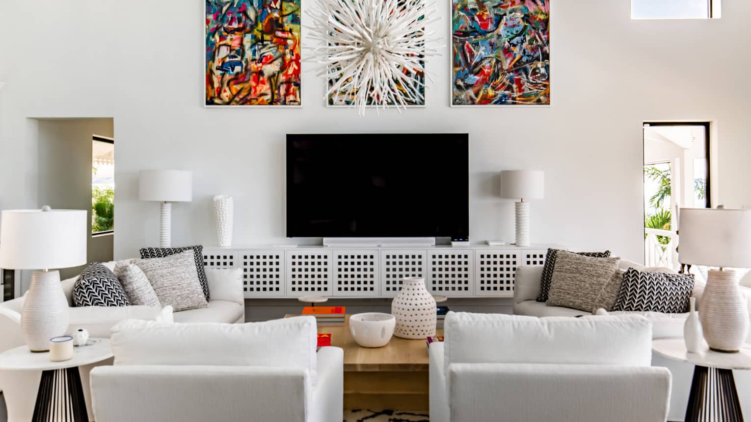Living room with two white sofas, two white armchairs, TV and three artwork
