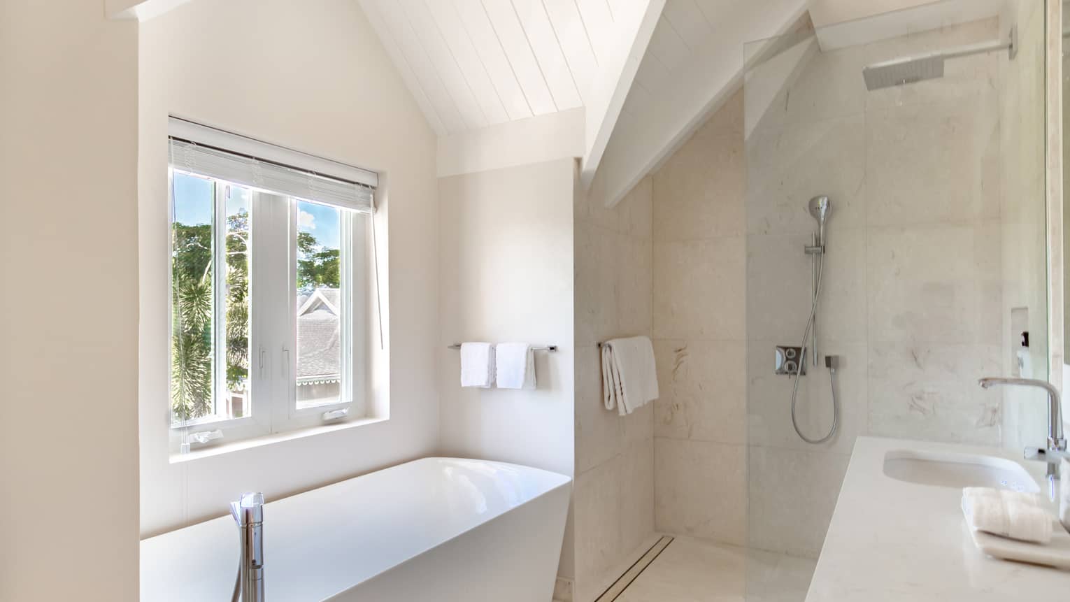 Light-coloured marble bathroom with walk-in glass shower, separate tub, window and double vanity